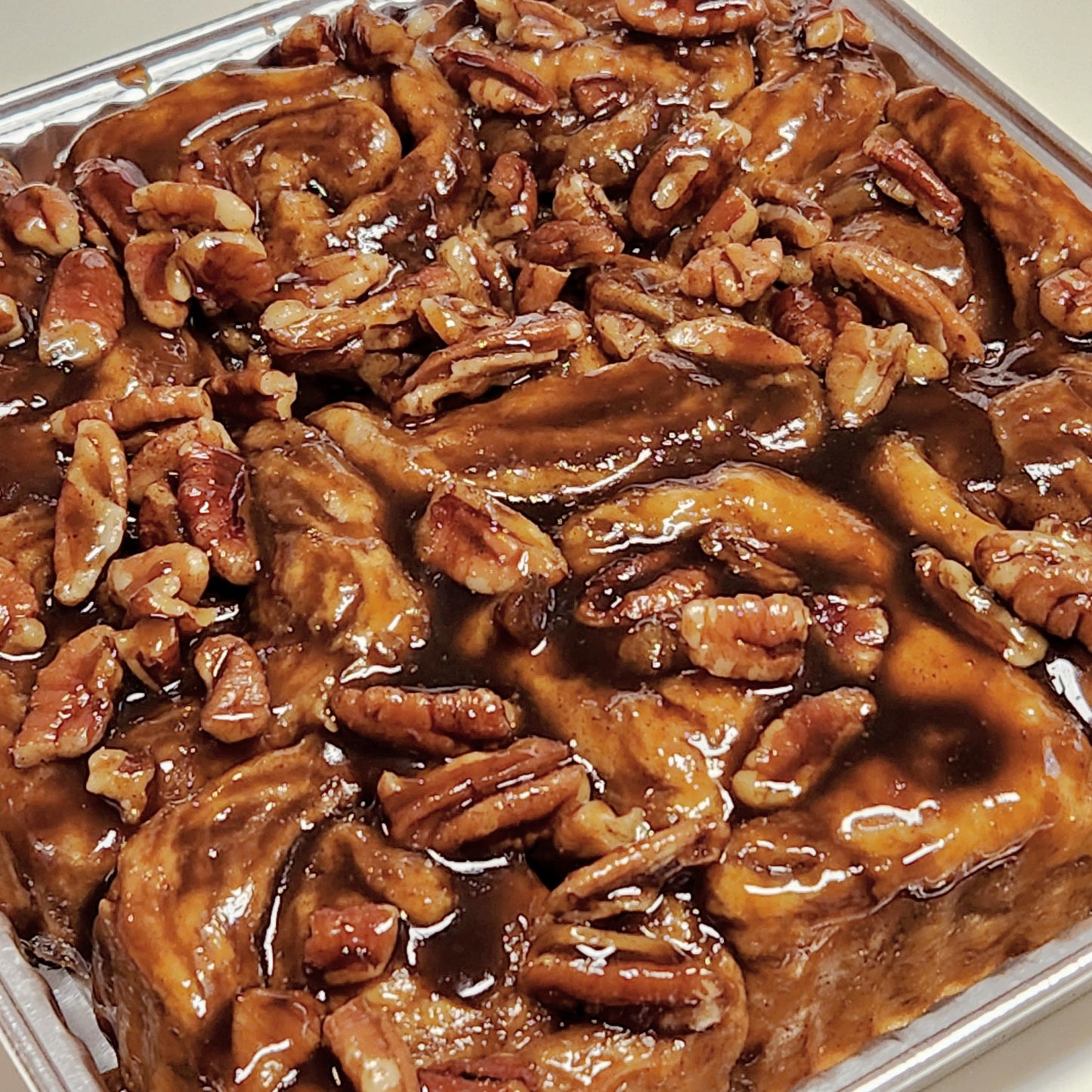 A close-up view of a tray of sticky caramel pecan rolls. The rolls are generously topped with glossy caramel sauce and a large amount of chopped and whole pecans, creating a rich, indulgent appearance.