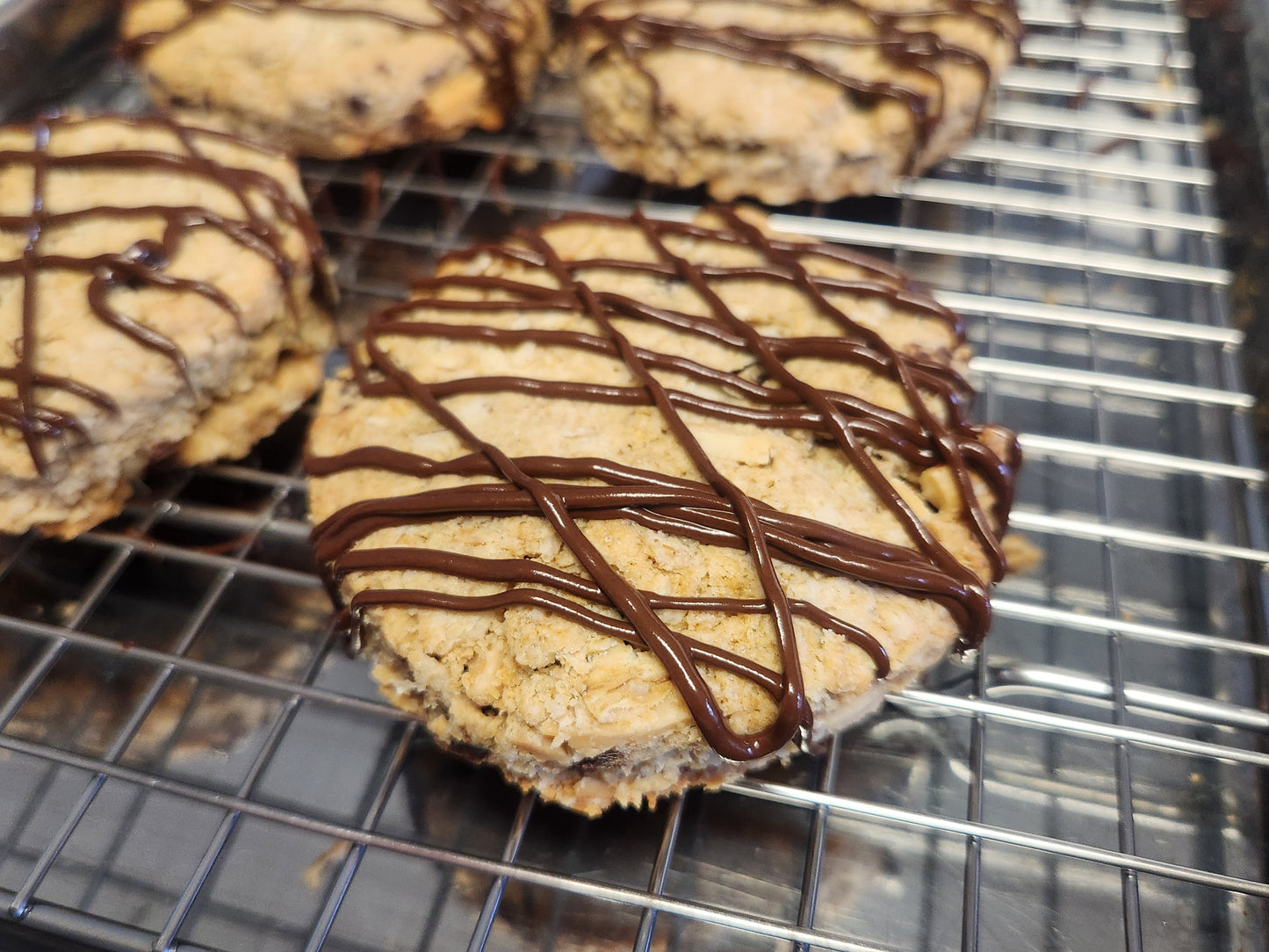 Close-up of gluten-free oat scones drizzled with dark chocolate, cooling on a wire rack. The scones have a golden-brown, crumbly texture with visible oats and a rich chocolate topping.