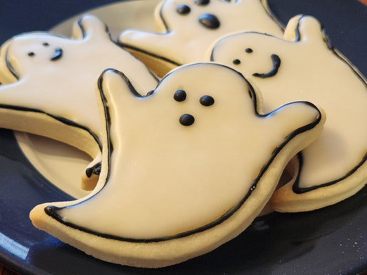 Gluten-free ghost-shaped cookies with black outlines on a dark plate