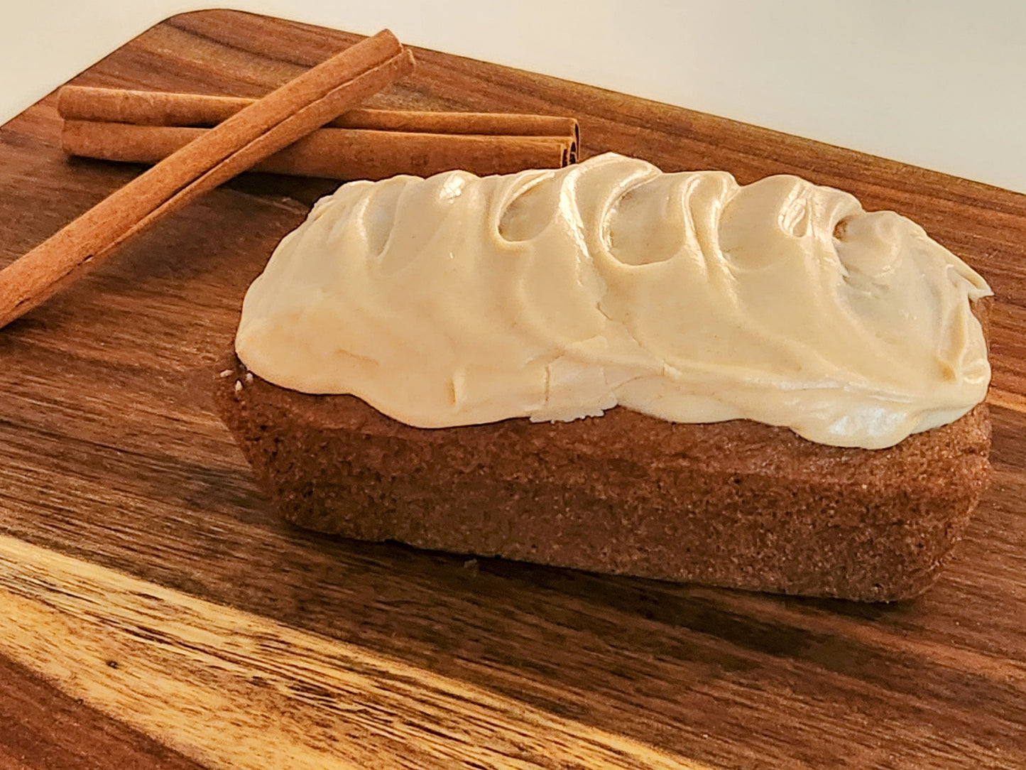 Gluten-free Pumpkin Mini Loaf with cinnamon cream cheese frosting on a brown cutting board with cinnamon sticks in the background